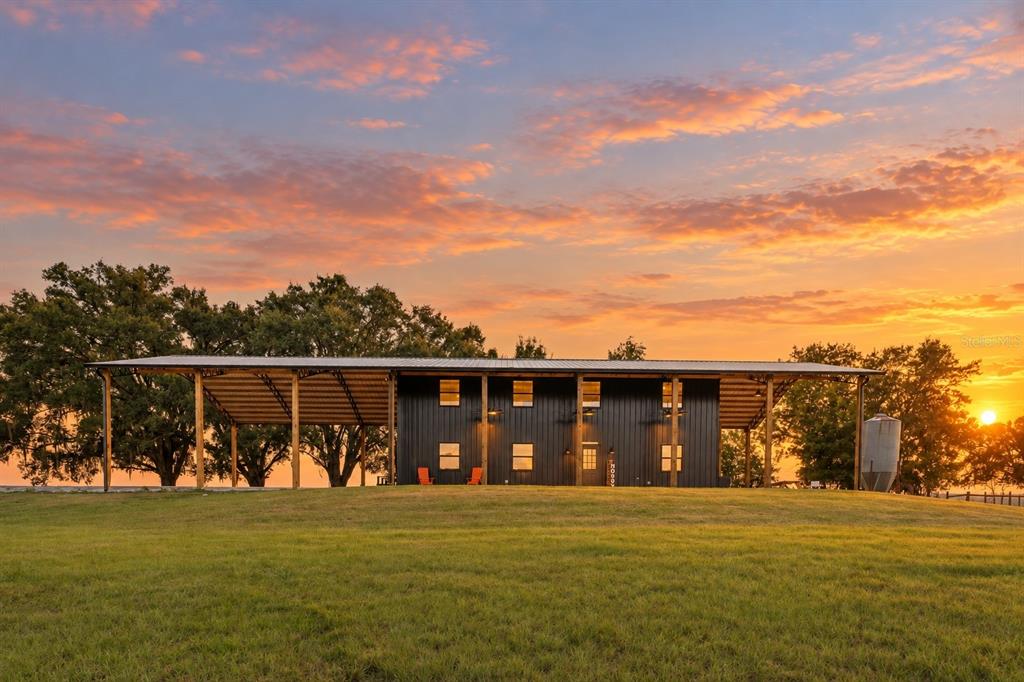 A black metal building with an attached open-sided carport sits on a grassy hill — 23220 NW 27TH ST, MORRISTON, FL