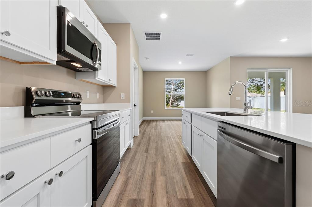 A modern kitchen features white cabinets, stainless steel appliances, and a central island with sink — 105 SELMA TRAIL, PALM COAST, FL