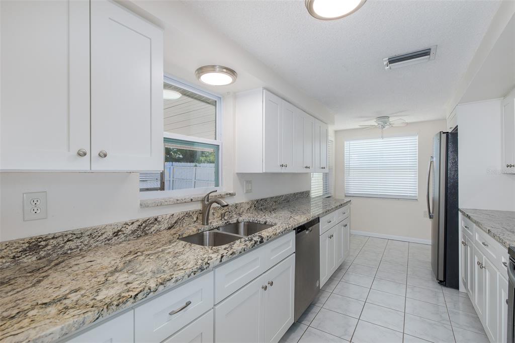 A kitchen with white cabinets, granite countertops, stainless steel appliances, and light tile flooring — 1148 FERNWOOD DRIVE, HOLIDAY, FL