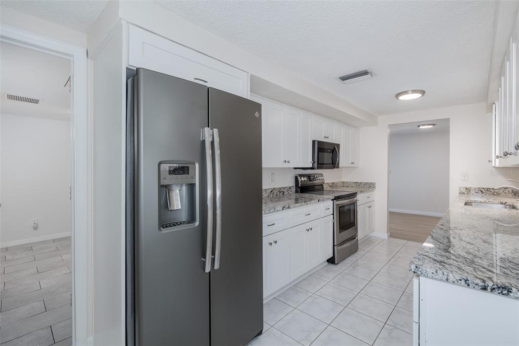 A kitchen featuring white cabinets, granite countertops, stainless steel appliances, and light-colored tile flooring — 1148 FERNWOOD DRIVE, HOLIDAY, FL