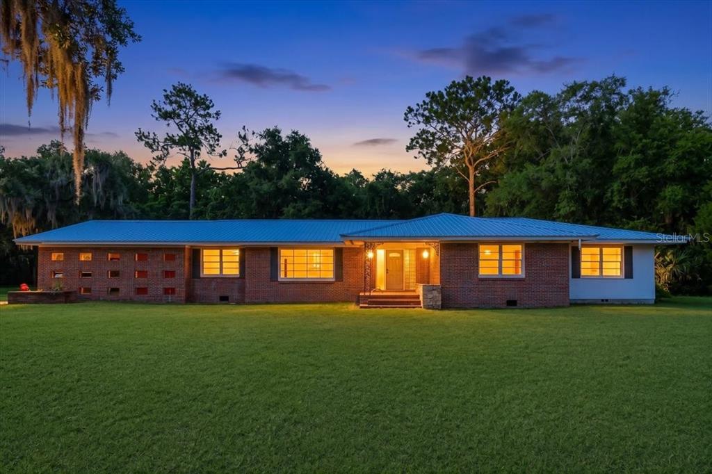 A single-story brick house with a metal roof sits on a large lawn at dusk — 2107 GOLF DRIVE, PALATKA, FL