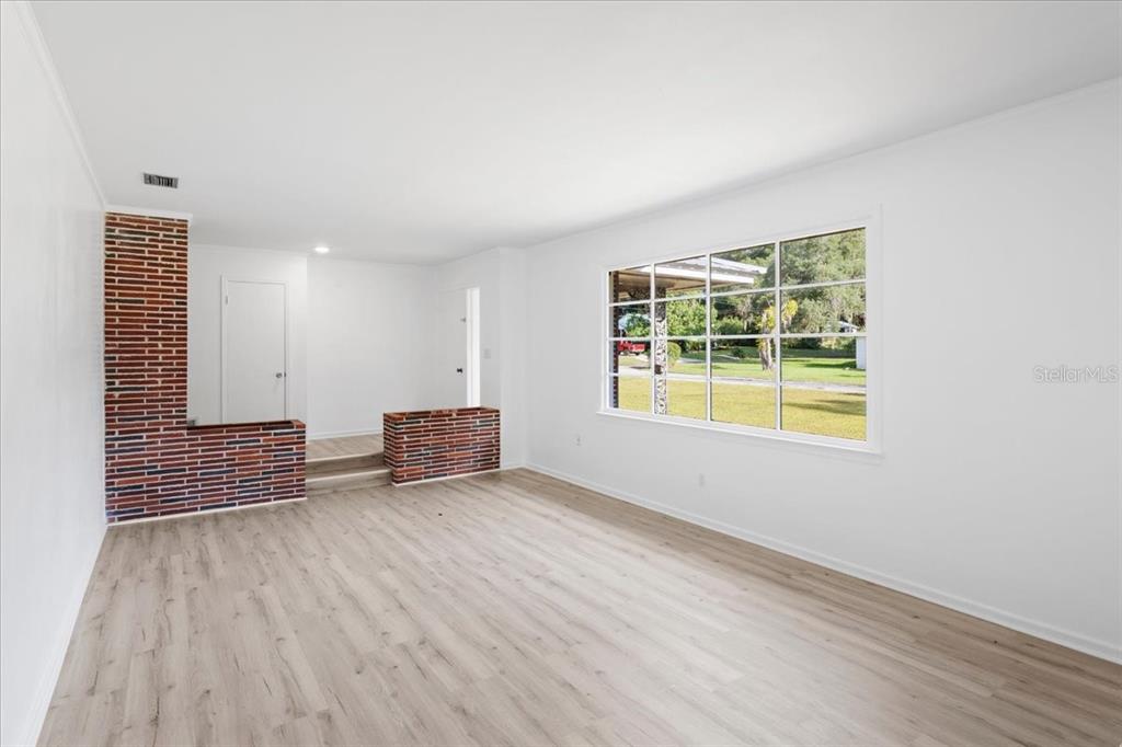 A living room features light wood-look flooring, white walls, and a decorative brick accent wall — 2107 GOLF DRIVE, PALATKA, FL