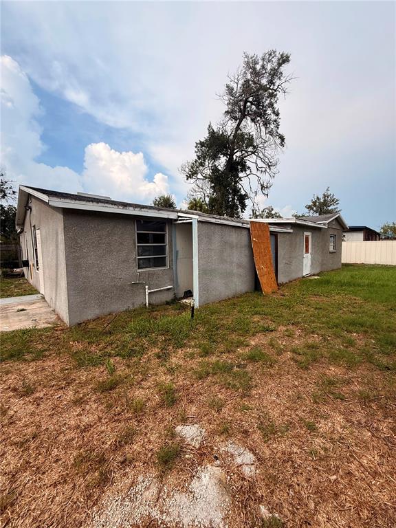 The exterior of a single-story gray stucco house with a piece of plywood covering a doorway — 806 W SHELL POINT ROAD, RUSKIN, FL