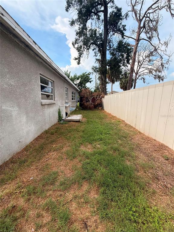 A side yard features a stucco house wall, a white fence, and a fallen tree — 806 W SHELL POINT ROAD, RUSKIN, FL