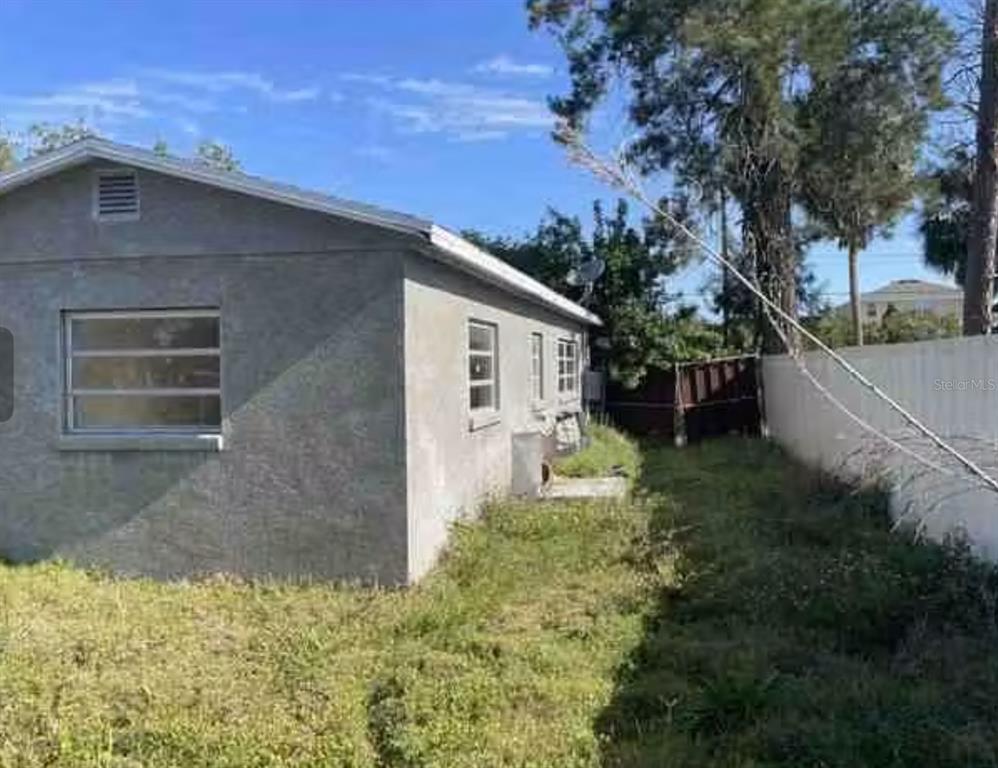 The exterior side of a gray stucco house features a window and a grassy yard — 806 W SHELL POINT ROAD, RUSKIN, FL