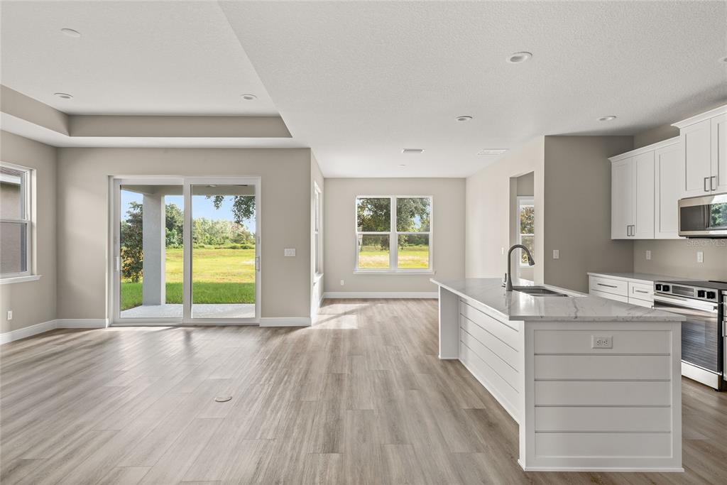A bright open-concept kitchen and living area with white cabinets, a kitchen island, and flooring — 3070 SUNSCAPE TERRACE, GROVELAND, FL