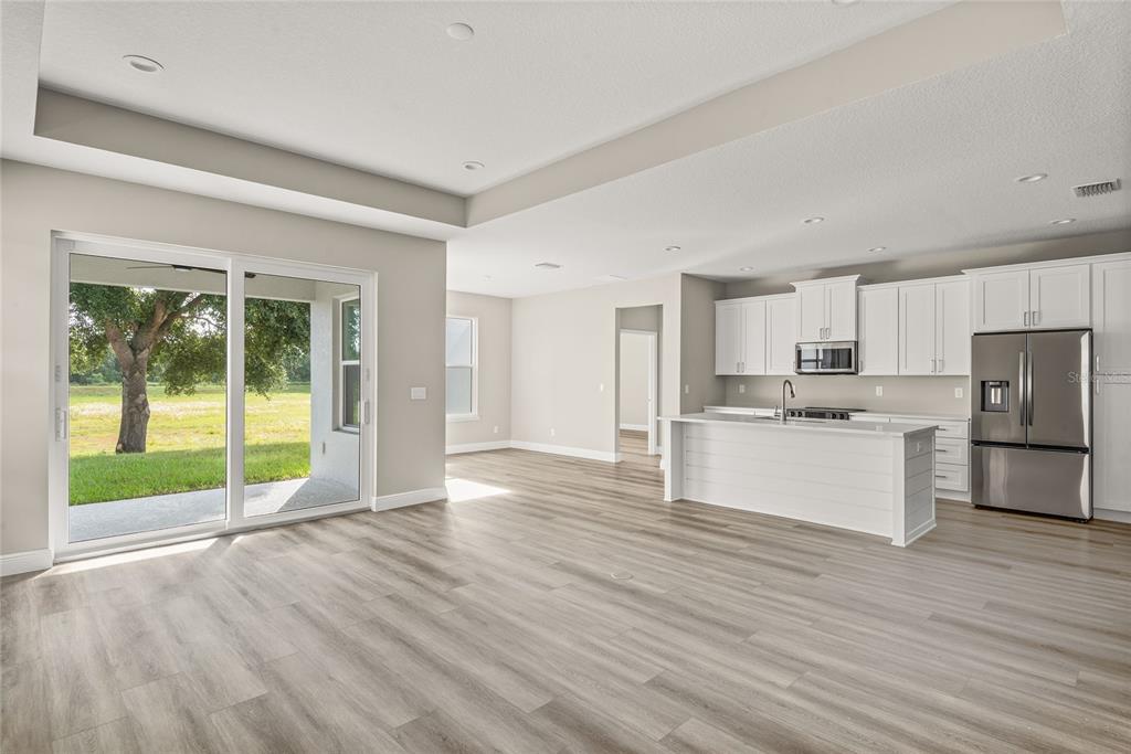 An open-concept kitchen and living area features white cabinetry, a kitchen island, and sliding doors — 3070 SUNSCAPE TERRACE, GROVELAND, FL