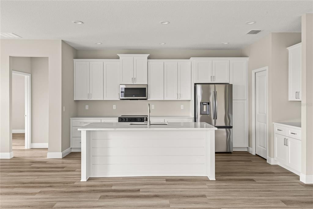 A modern kitchen features white cabinets, stainless steel appliances, a center island, and wood-look flooring — 3070 SUNSCAPE TERRACE, GROVELAND, FL