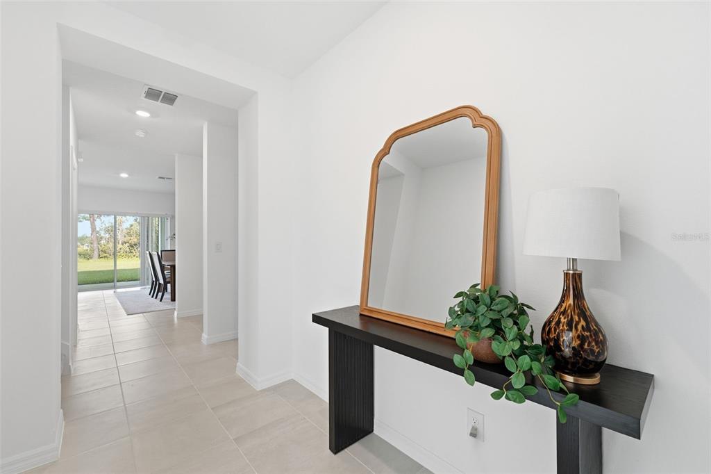 A hallway features a dark console table with a mirror, lamp, and plant against white walls — 748 FARFIELDS STREET, DELAND, FL