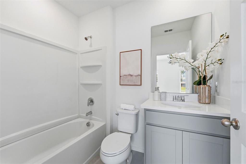 A bathroom features a white tub-shower combo, a toilet, and a gray vanity with mirror — 748 FARFIELDS STREET, DELAND, FL