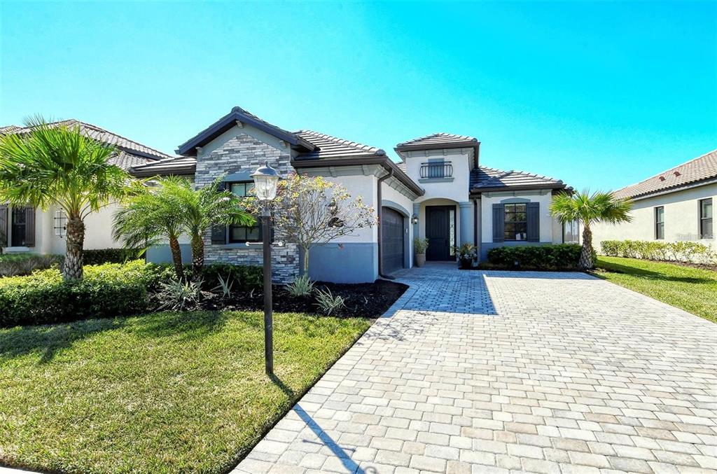 A single-story house with a stone facade, paver driveway, and palm trees in the front yard — 6132 CESSNA RUN, BRADENTON, FL