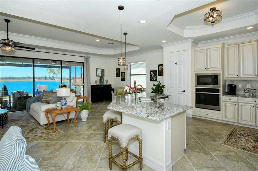 An open-concept kitchen and living area features granite countertops, light cabinetry, and a lake view — 6132 CESSNA RUN, BRADENTON, FL