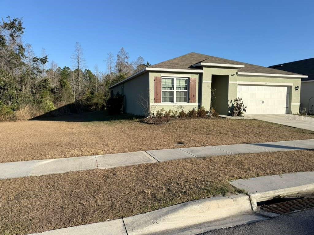 A single-story house with a light green exterior, brown shutters, and a two-car garage — 1415 FOX SQUIRREL DRIVE, DAVENPORT, FL