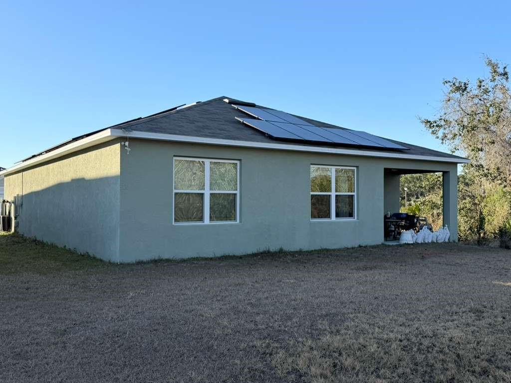 The exterior of a single-story house with stucco walls, a shingled roof, and solar panels — 1415 FOX SQUIRREL DRIVE, DAVENPORT, FL