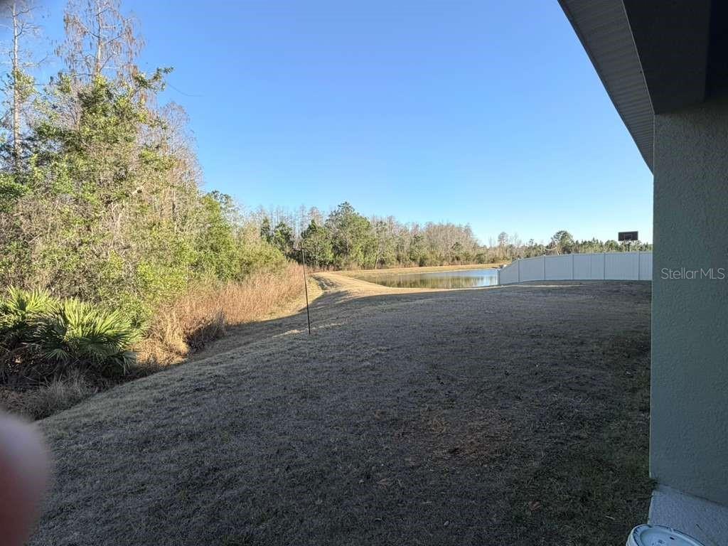 A grassy backyard slopes toward a pond bordered by trees and a white fence — 1415 FOX SQUIRREL DRIVE, DAVENPORT, FL