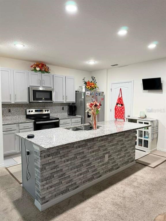 A kitchen features light gray cabinets, granite countertops, and a stone-accented center island — 1415 FOX SQUIRREL DRIVE, DAVENPORT, FL