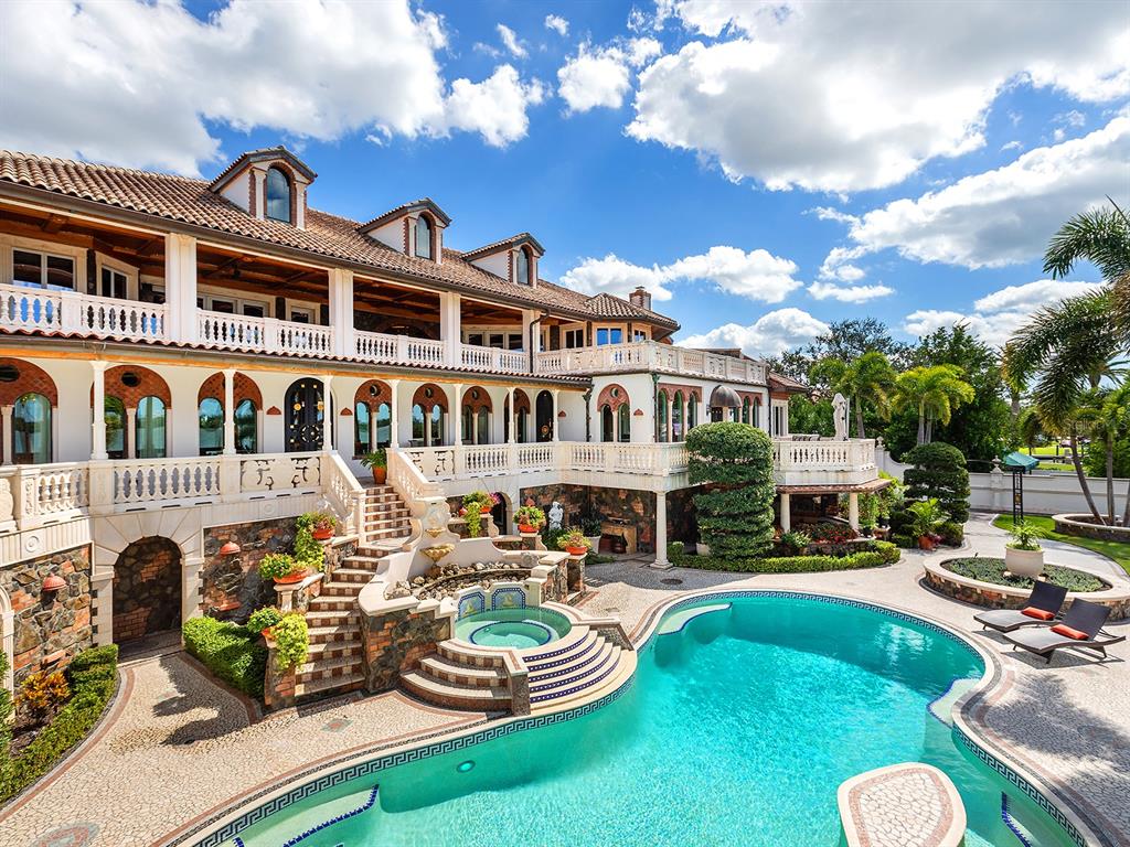 A luxury waterfront home features a tiered swimming pool, stone patio, and palm trees — 1310 S LAKE SHORE DRIVE, SARASOTA, FL