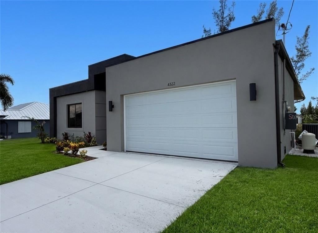 A modern, single-story house exterior features a gray stucco facade and a white garage door — 4322 KISMET PARKWAY W, CAPE CORAL, FL