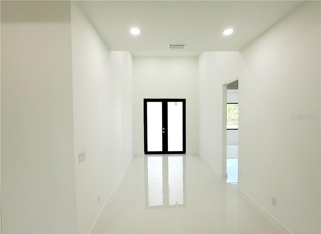 A bright, minimalist hallway features white walls, glossy tile flooring, and black-framed double doors — 4322 KISMET PARKWAY W, CAPE CORAL, FL