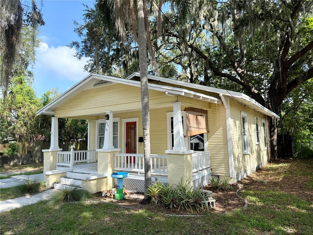 A yellow, single-story bungalow with a front porch, white railings, and large oak trees — 521 YOUNG PLACE, LAKELAND, FL