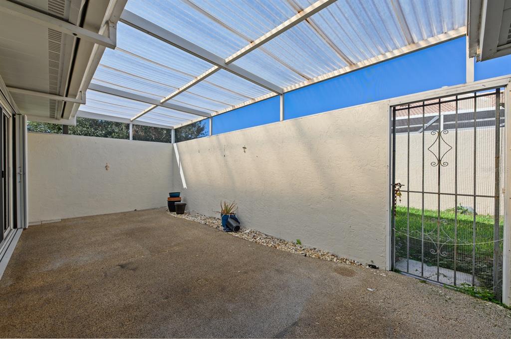 A covered concrete patio features white stucco walls and a metal security gate — 5528 37TH STREET E UNIT 5528, BRADENTON, FL