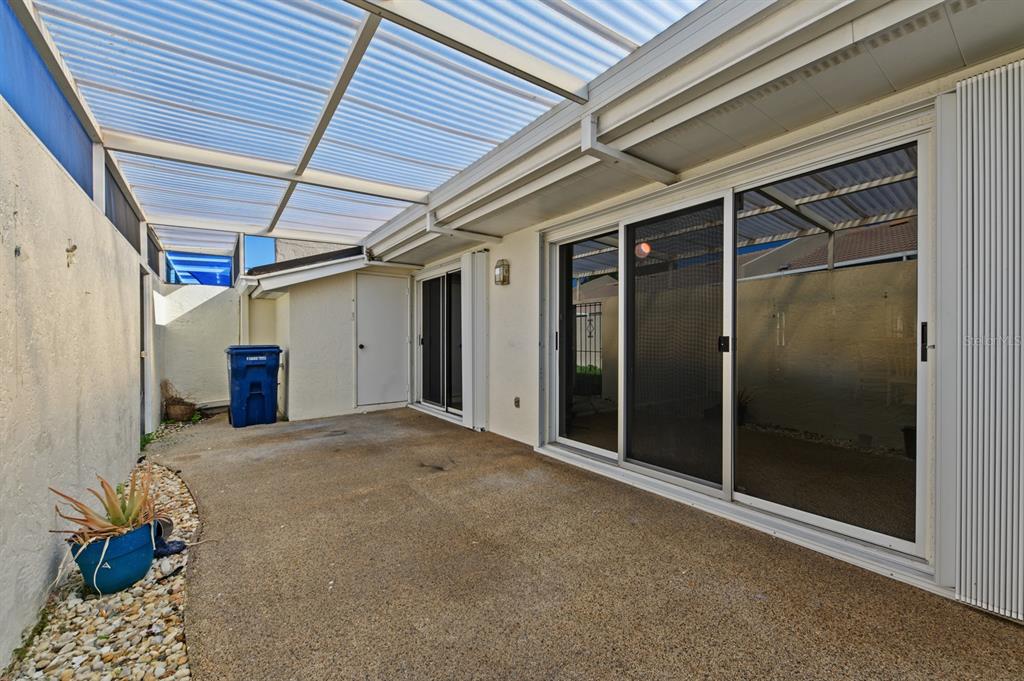 A covered concrete patio features a sliding glass door and a blue trash bin — 5528 37TH STREET E UNIT 5528, BRADENTON, FL