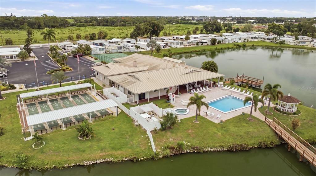 An aerial view of a community clubhouse featuring a pool, shuffleboard courts, and a lake — 2215 73RD STREET E UNIT 162, PALMETTO, FL