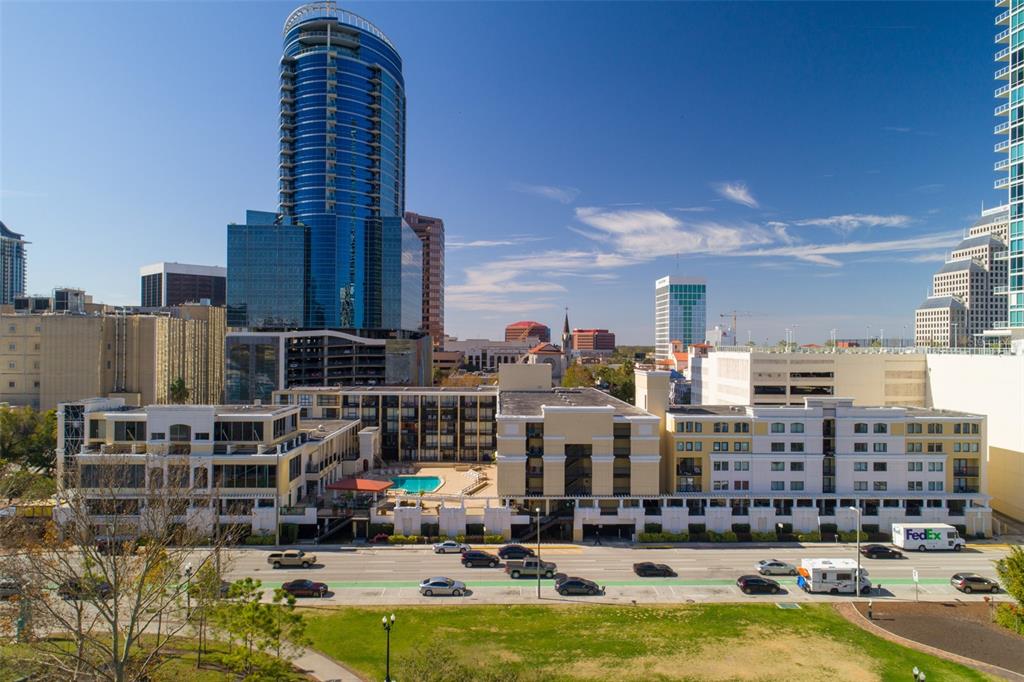 An exterior view of a multi-story apartment complex with a pool and city skyline — 151 E WASHINGTON STREET UNIT 209, ORLANDO, FL