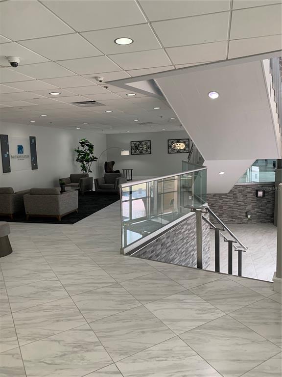 A modern lobby features marble-look tile flooring, a glass-railed staircase, and a seating area — 151 E WASHINGTON STREET UNIT 209, ORLANDO, FL