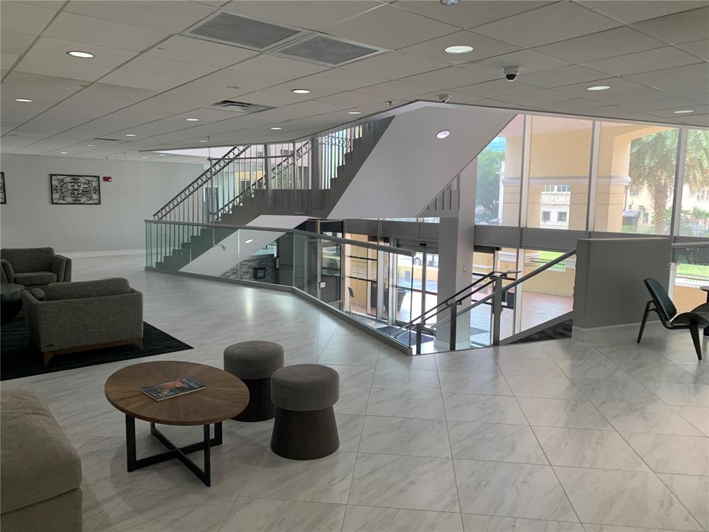 A modern lobby features marble-look tile flooring, a glass-railed staircase, and comfortable lounge seating — 151 E WASHINGTON STREET UNIT 209, ORLANDO, FL
