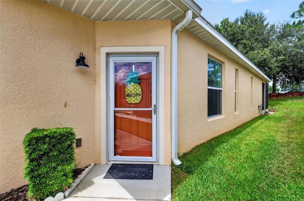 A beige stucco house exterior features a white storm door with a pineapple welcome sign — 26951 WHITE PLAINS WAY, LEESBURG, FL