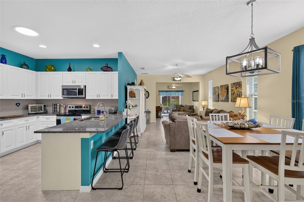 An open-concept kitchen and dining area features white cabinets, teal walls, and tile flooring — 26951 WHITE PLAINS WAY, LEESBURG, FL