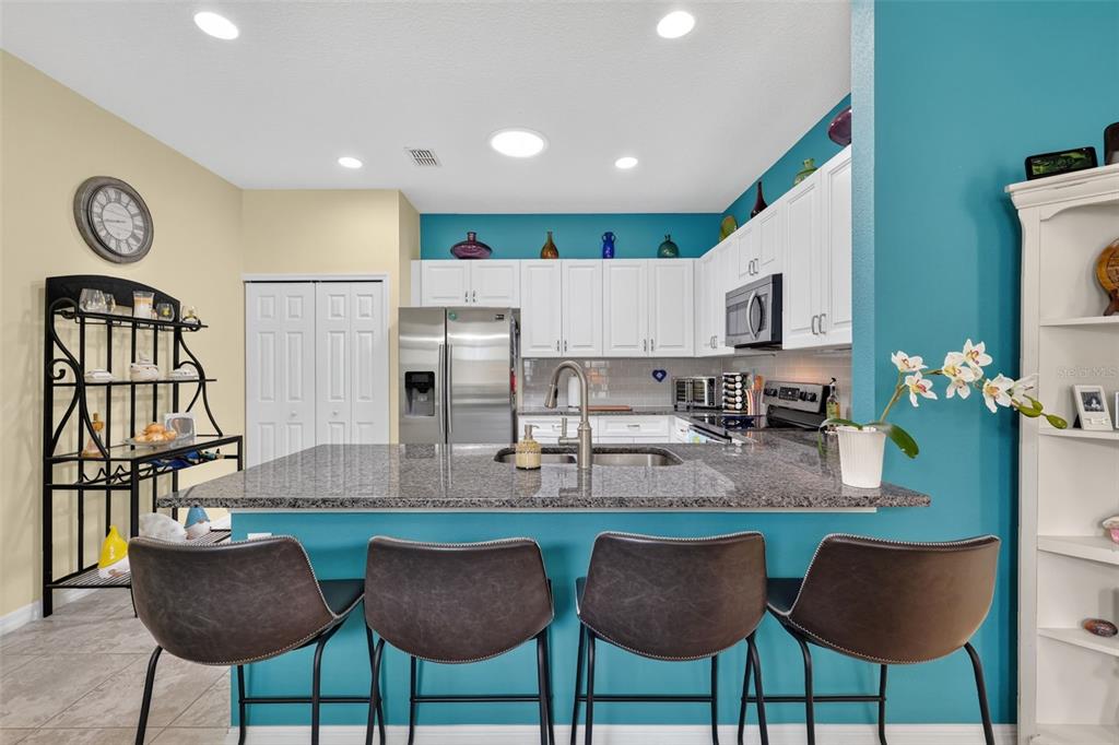 A kitchen features a granite-topped island, white cabinetry, and teal walls with four bar stools — 26951 WHITE PLAINS WAY, LEESBURG, FL