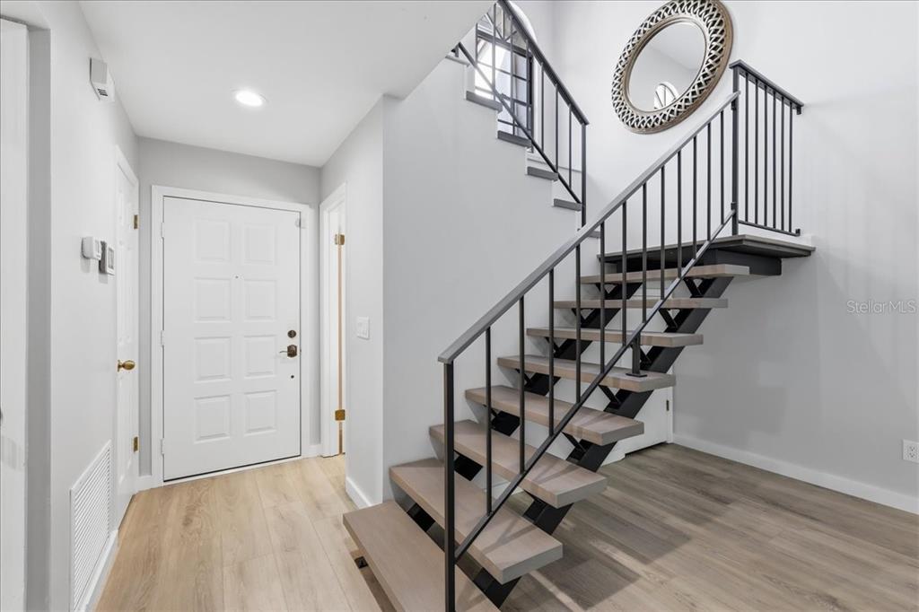 An entryway features light wood flooring, a white front door, and a modern open-tread staircase — 7537 FENWICK COVE LANE, ORLANDO, FL