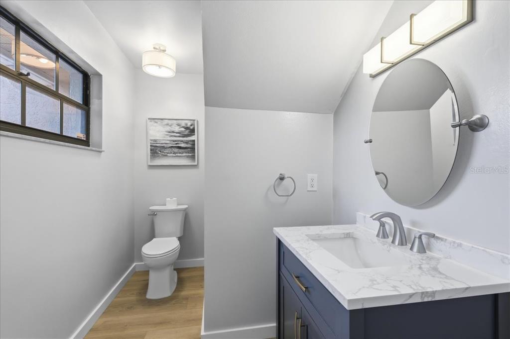 A bathroom features a dark blue vanity, a round mirror, and a toilet on wood flooring — 7537 FENWICK COVE LANE, ORLANDO, FL