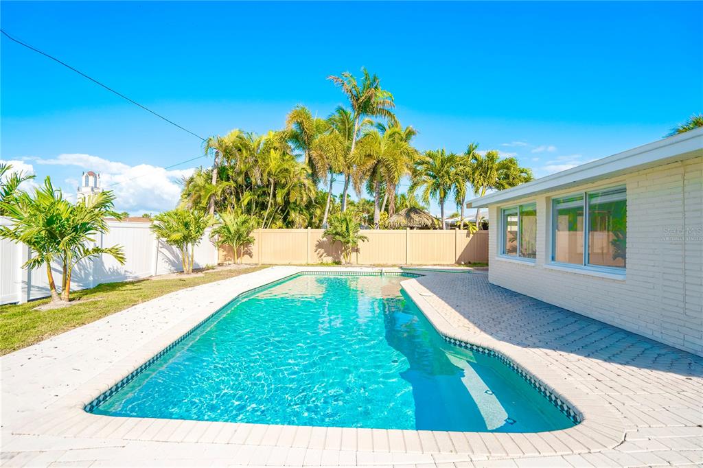 A backyard features a rectangular swimming pool, a paved patio, and several palm trees — 455 81ST AVENUE, ST PETE BEACH, FL