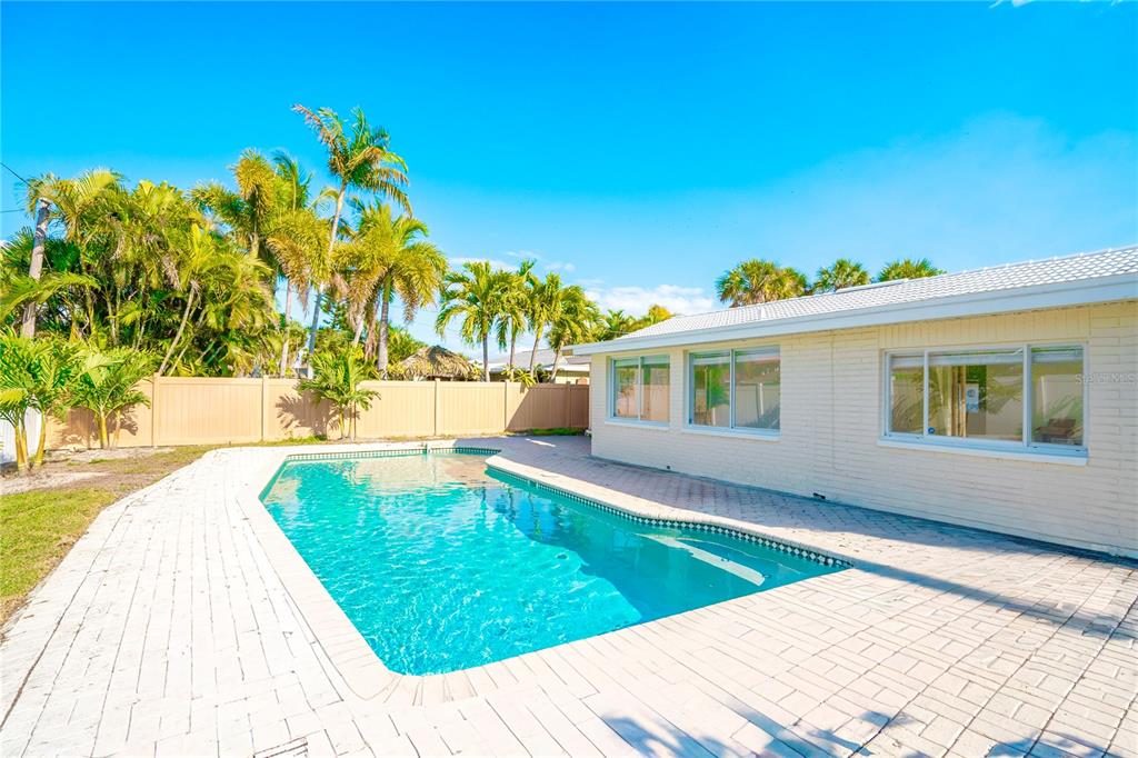 A backyard features a swimming pool surrounded by a brick patio and palm trees — 455 81ST AVENUE, ST PETE BEACH, FL