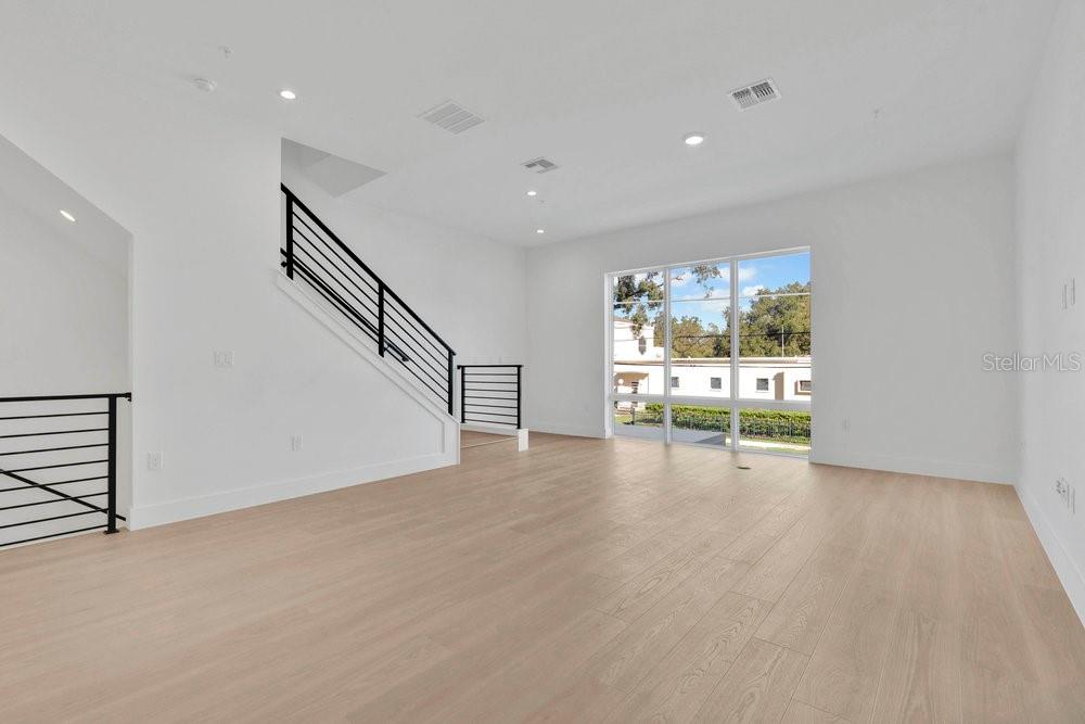 A bright living room features light wood flooring, white walls, and a modern staircase — 1004 E ROBINSON, ORLANDO, FL