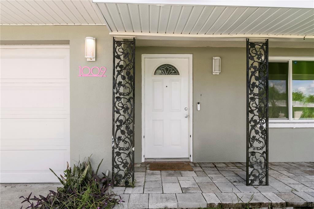 The exterior of a home features a white front door, decorative metal columns, and pavers — 1009 WOODLEY ROAD, CLEARWATER, FL