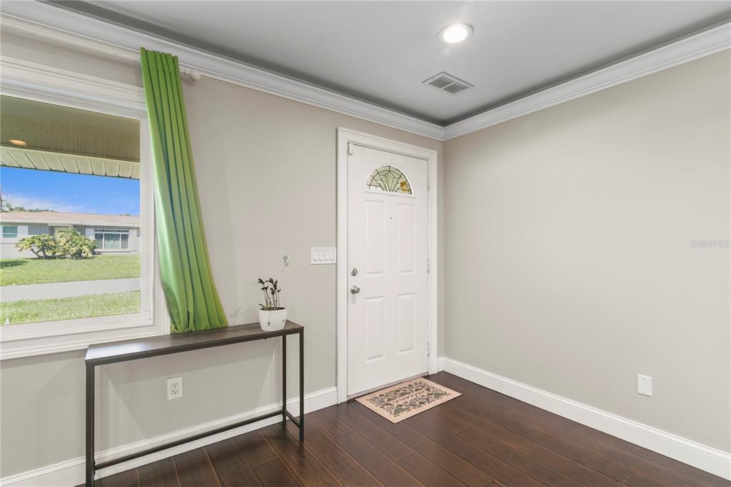 An entryway features dark wood flooring, a white front door, and a console table — 1009 WOODLEY ROAD, CLEARWATER, FL