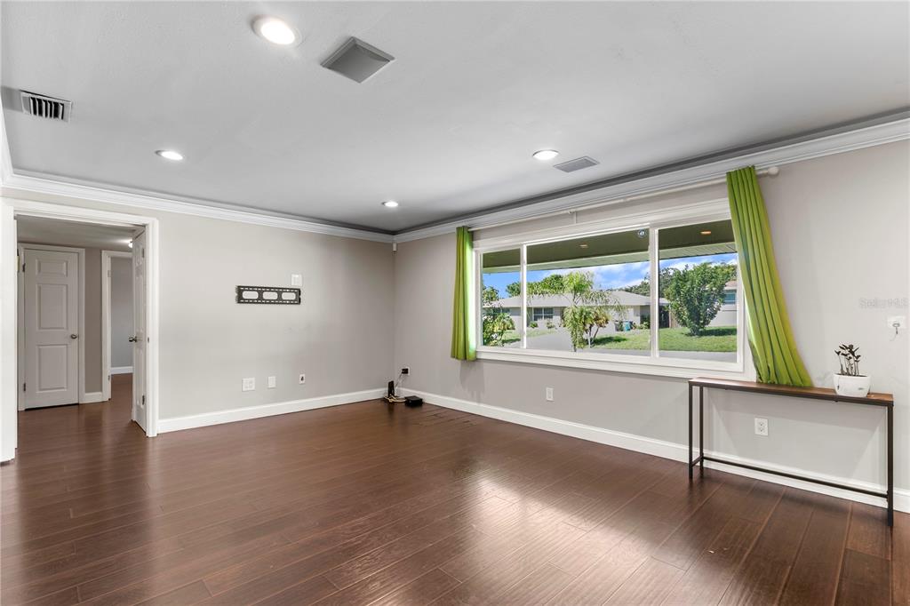 An empty living room features dark wood flooring, light gray walls, and a large window — 1009 WOODLEY ROAD, CLEARWATER, FL