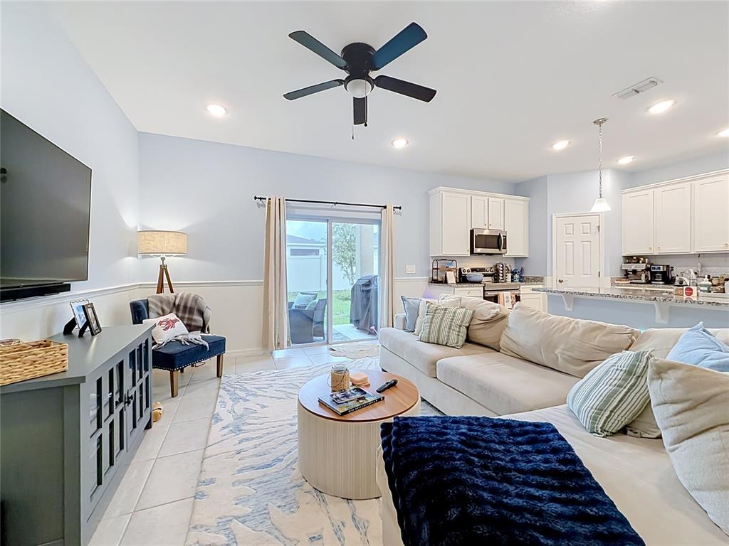 An open-concept living room features a sectional sofa, a television, and an adjoining kitchen area — 3947 MAYHILL LOOP, EUSTIS, FL