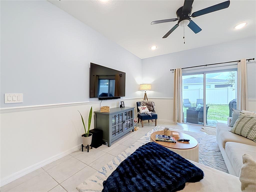 A living room features light blue walls, white wainscoting, a ceiling fan, and sliding glass doors — 3947 MAYHILL LOOP, EUSTIS, FL