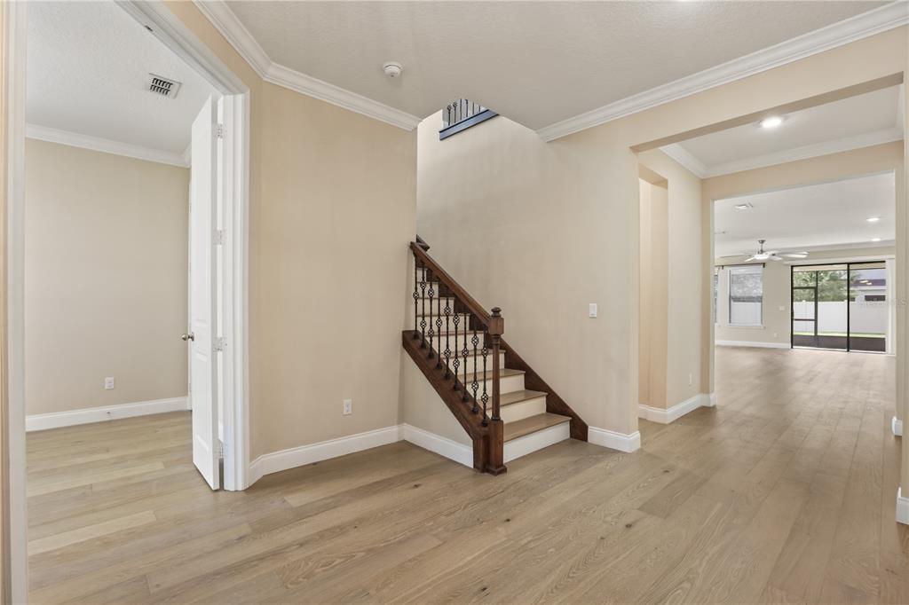 An interior view of a foyer featuring light wood flooring, a staircase, and open doorways — 8278 PROCIDA ISLE LANE, WINDERMERE, FL
