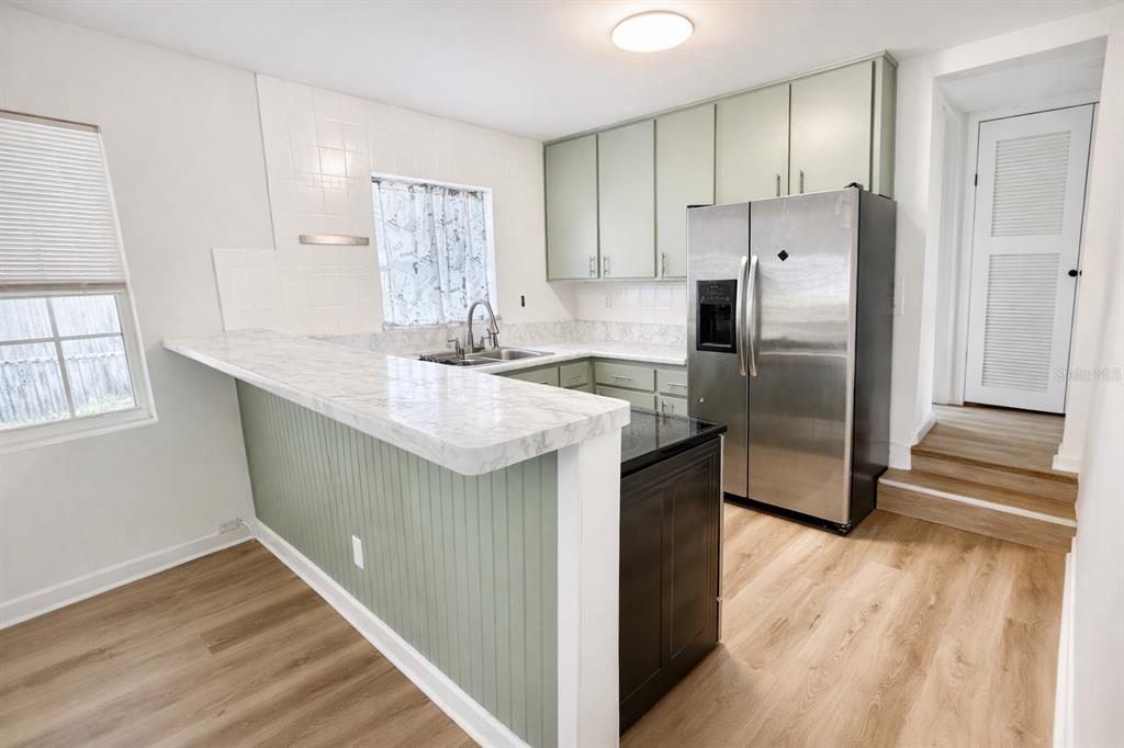 A kitchen features sage green cabinets, a marble-look breakfast bar, and stainless steel appliances — 4128 ARCOT CIRCLE, JACKSONVILLE, FL