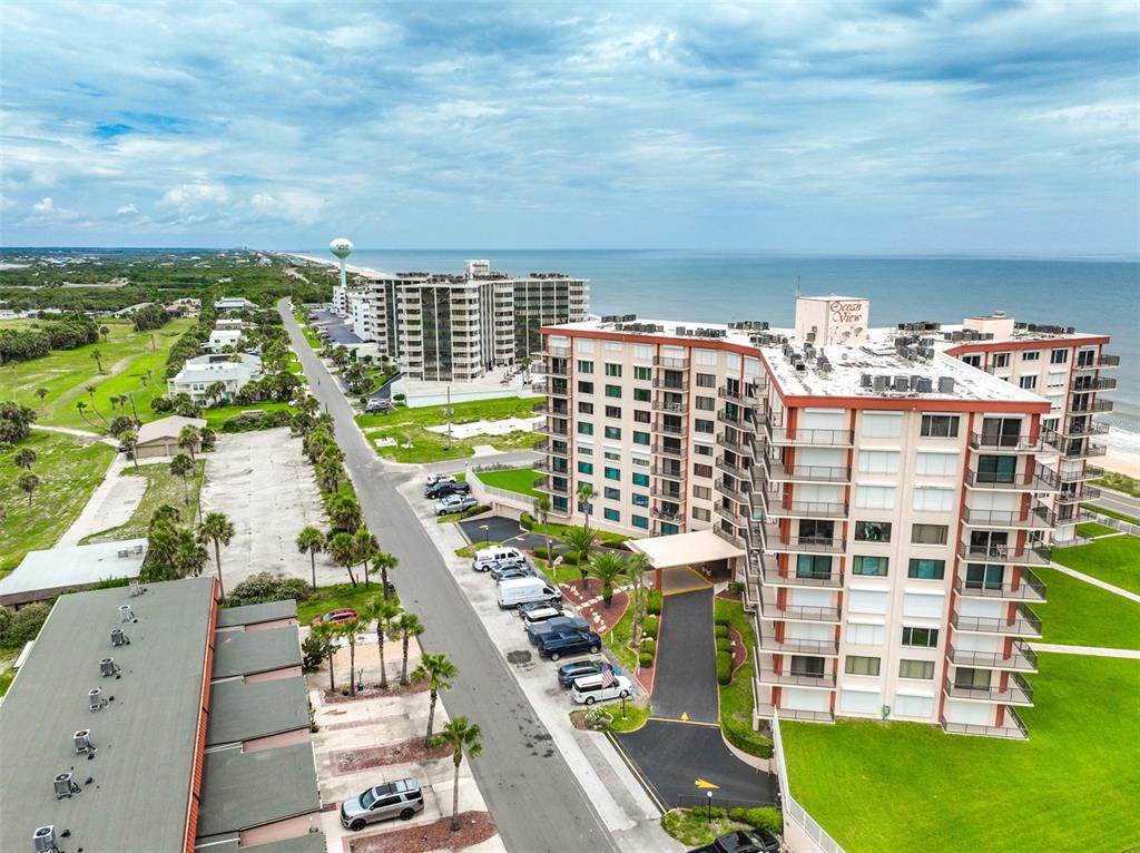 An aerial view shows a multi-story apartment building with balconies near a coastal road — 3600 S OCEAN SHORE BOULEVARD UNIT 222, FLAGLER BEACH, FL
