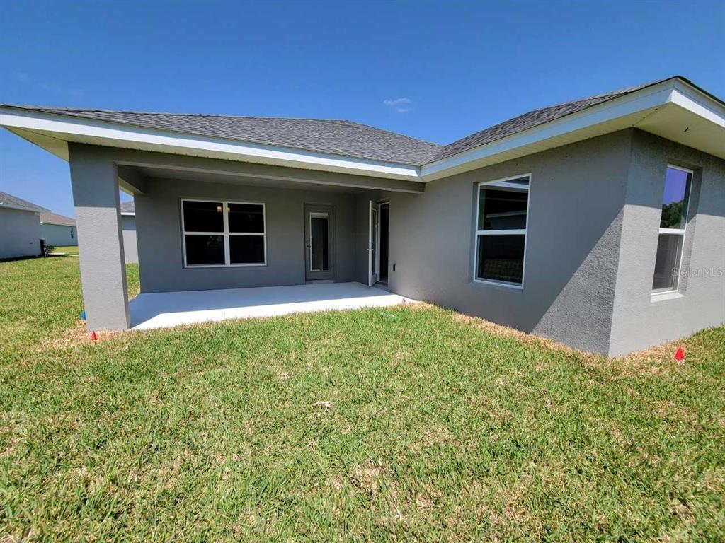 A view of a house exterior featuring a covered patio and a grassy backyard — 4493 SW 91ST LANE ROAD, OCALA, FL