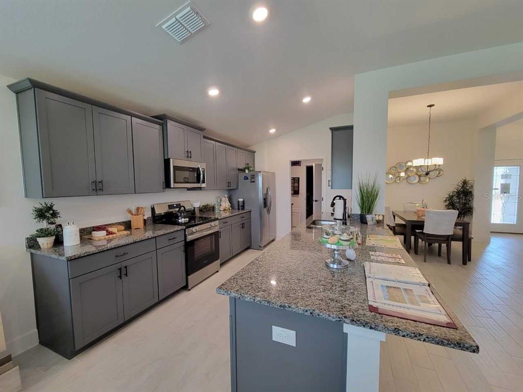A kitchen features gray cabinets, granite countertops, a large island, and stainless steel appliances — 4493 SW 91ST LANE ROAD, OCALA, FL