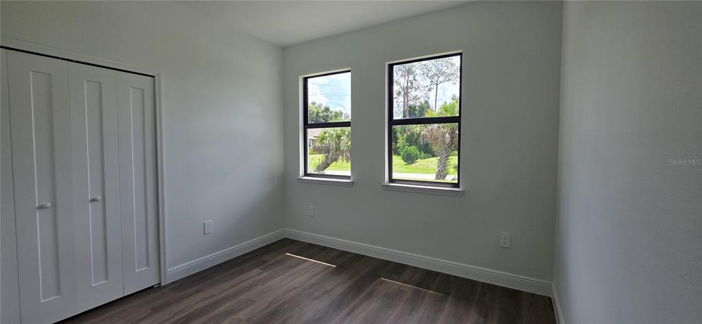 An empty bedroom features light gray walls, dark wood-look flooring, and two windows — 1267 HENNING STREET, NORTH PORT, FL