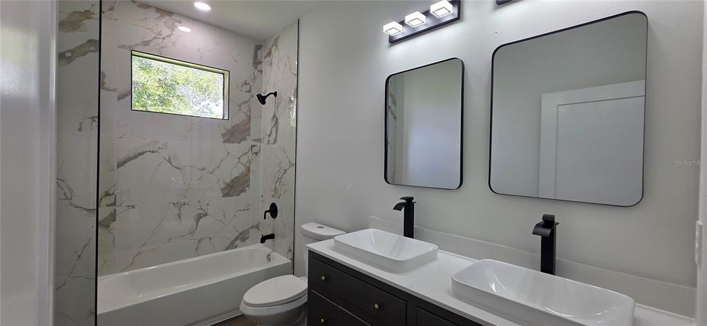 A bathroom features a double vanity with black faucets, rectangular mirrors, and a tiled tub-shower — 1267 HENNING STREET, NORTH PORT, FL